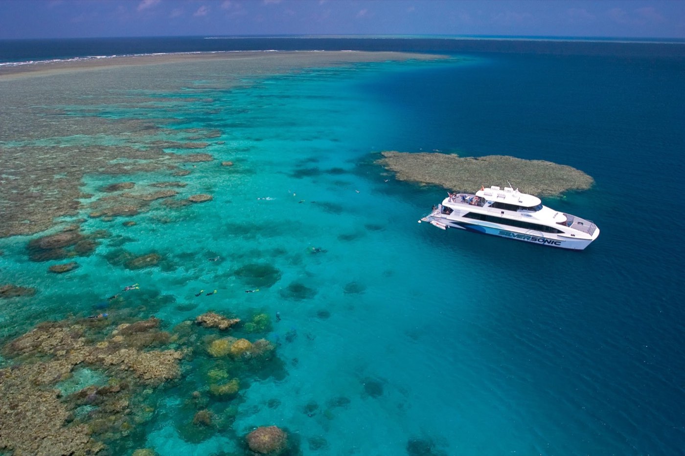 A dive boat moored at a coral reef with snorkellers in the water